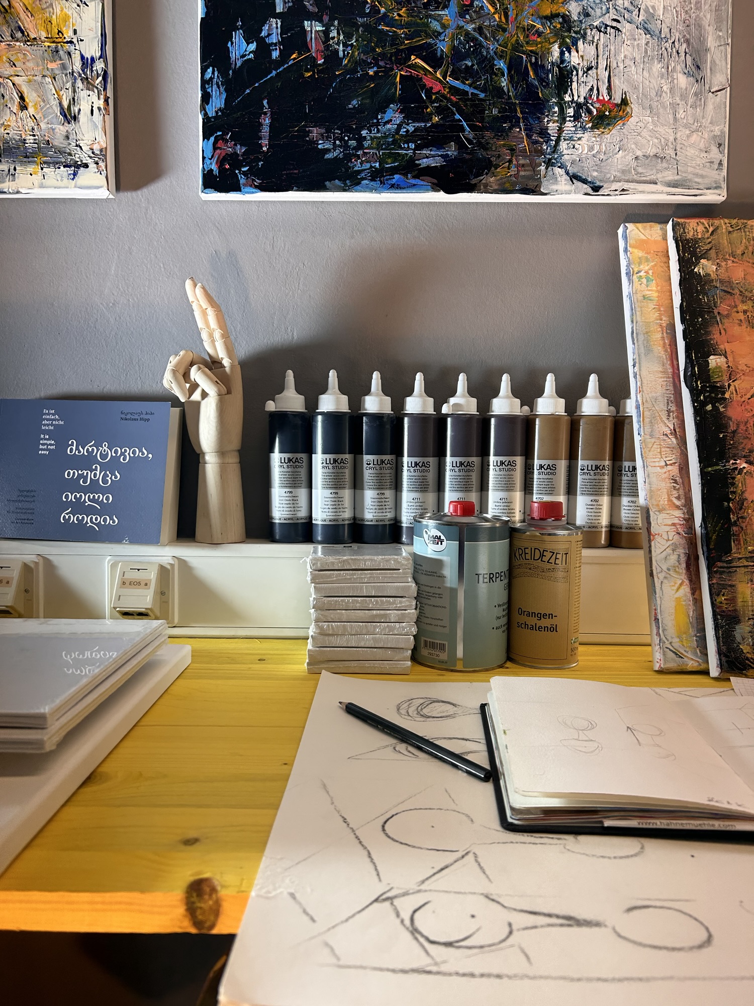 Atelier von Leonhard Gürtner — Acrylfarben, Skizzenbuch und gerahmte Werke an der Wand